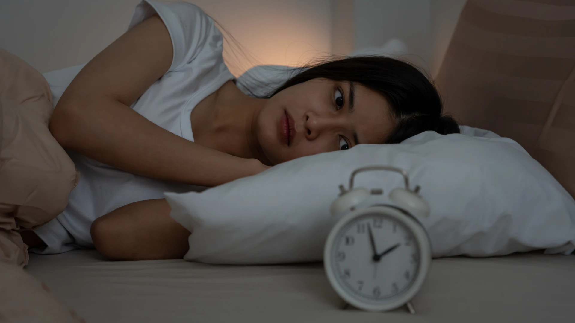 A person lying awake in bed at night with a bedside clock showing an early morning hour, illustrating Lyme disease insomnia