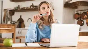 woman at a kitchen table with a laptop and a notebook of questions, preparing for a video visit with a Lyme doctor